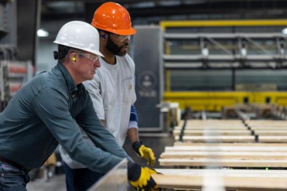 2 men one in white hat and other in orange shown working in a manufacturing unit wearing hard hat